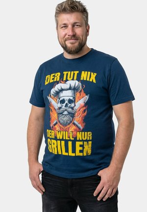 Mężczyzna z brodą w granatowej koszuli z płonącą czaszką w czapce kucharskiej i skrzyżowanymi nożami, z niemieckim tekstem o grillowaniu.