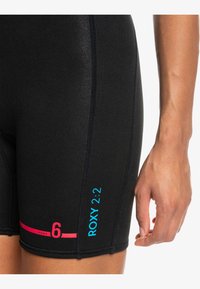 Shorts de combinaison noirs avec des marquages "ROXY" en rose et bleu, dotés de coutures à plat et d'un ajustement serré pour les activités nautiques.