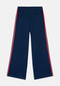 Mornarskoplave mrežaste hlače širokih nogavica, s crvenim i bijelim okomitim bočnim prugama. Elastični pojas za prilagodljivo pristajanje.