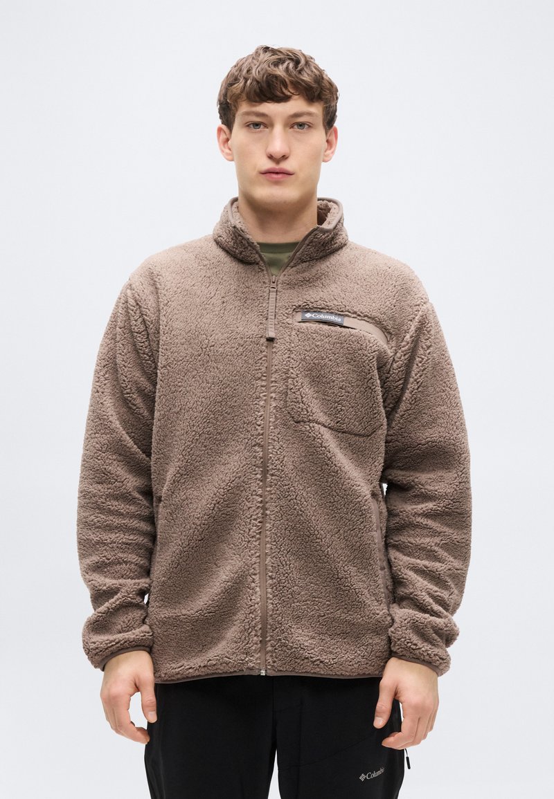 Καφέ φλις μπουφάν με φερμουάρ στο μπροστινό μέρος, ψηλό γιακά και τσέπη στο στήθος. Διαθέτει μαλακή, υφή και ελαστικά μανίκια.