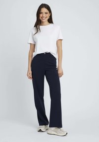 T-shirt blanc à col rond associé à un pantalon large bleu marine. Le pantalon dispose d'une fermeture à bouton et de poches avant. Coupe ajustée au corps.