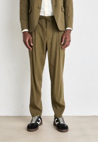 Olive green, lightweight linen blend pants with a drawstring waist, featuring a relaxed fit, paired with black and white sneakers.