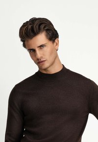 Brązowy sweter robiony na drutach z wysokim kołnierzem, dopasowanym krojem i długimi rękawami, o gładkiej teksturze i minimalistycznym stylu.