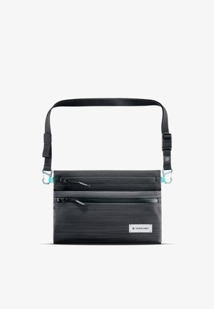 Sac bandoulière noir en tissu avec deux compartiments zippés, sangle ajustable et accent bleu clair sur le matériel. Étiquette de marque visible.