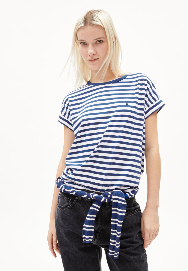 Striped t-shirt in navy blue and white cotton with rolled sleeves, paired with high-waisted black jeans and a tied blue-accented belt.