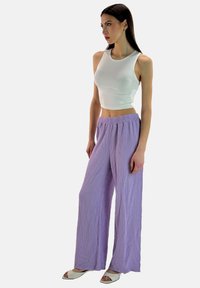 Witte cropped tanktop gecombineerd met losse paarse gekreukte stoffen broek, met een elastische tailleband en wijde benen.