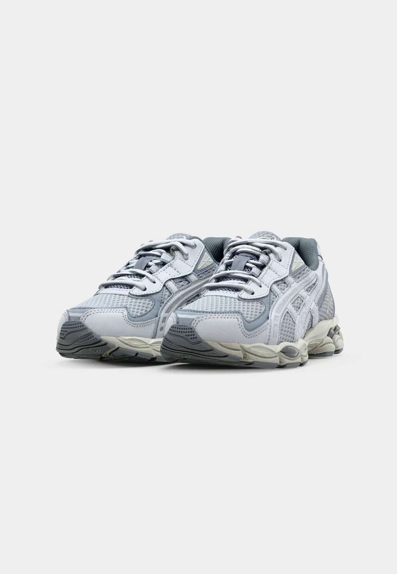 Hellgraue Sportschuhe mit Mesh-Obermaterial, gepolsterten Zungen und strukturierten Gummisohlen. Sie verfügen über weiße Akzente und ein klobiges Design.