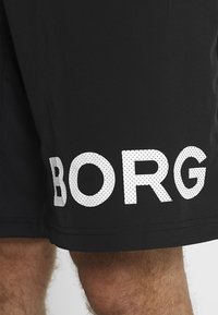 Čierne športové šortky vyrobené z ľahkého materiálu, s veľkým bielym perforovaným logom "BORG" na ľavej nohe.
