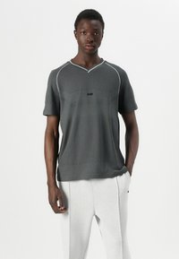 Gray short-sleeve shirt with a textured fabric, V-neck, and white accents. Features a logo on the chest and a relaxed fit.