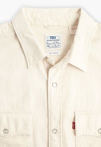 Relaxed-fit cream western shirt made of thick cotton fabric. Features a pointed collar, pocket with snap detail, and brand label inside.