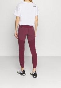 Avskuren vit t-shirt med logotyp på baksidan, kombinerad med burgundy leggings med kontrasterande paneler och svart-vita sportskor.