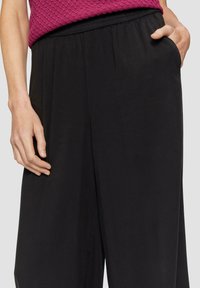 Zwarte wijde broek met een elastische tailleband, zijzak en een gladde textuur, gecombineerd met een gemêleerd magentakleurig topje.