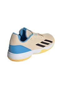 Zapatilla deportiva de malla beige con acentos azules, logo de raya negra y suela de goma amarilla. Presenta una parte superior texturizada y un cuello acolchado.