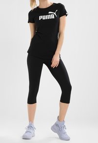 T-shirt en coton noir avec logo "PUMA" blanc, associé à un legging noir et des chaussures de sport bleu clair au design moderne.