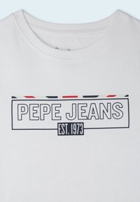 Camiseta blanca de algodón con un gráfico en negro que dice "PEPE JEANS" con acentos horizontales en rojo y negro y "EST. 1973" en una fuente más pequeña.