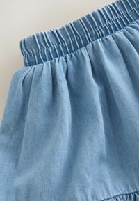 Jupe en denim bleu clair avec une taille élastique froncée et des volants superposés. Le tissu présente une texture lisse avec un motif de tissage subtil.