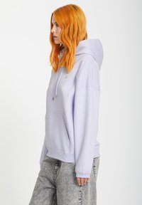 Lila hoodie met een voorzak, trekkoord en geribbelde manchetten, gecombineerd met grijze gemusterde broek. Soepele stoftextuur.