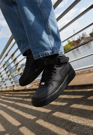 Mustad mustad Nike Air Force 1 sneakerid nahast pealsega, mestist keelaga ja kummist tallaga, millel on kõrge disain ja paksud paelad.