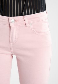 Jeans de cáñamo rosa claro con un diseño de cinco bolsillos, cierre frontal con botón y una textura suave. Presenta costuras sutiles y detalles de metal.