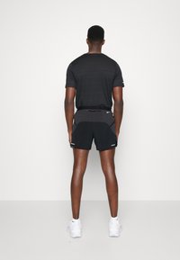 Pantalones cortos deportivos negros con una cintura texturizada gris, combinados con una camiseta de manga corta gris oscuro; zapatillas blancas completan el look.
