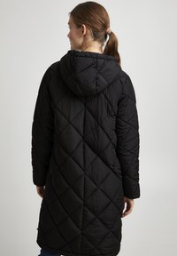 Cappotto lungo trapuntato nero con cappuccio, caratterizzato da un motivo a diamante, una texture morbida e tasche laterali. Design semplice con vestibilità rilassata.