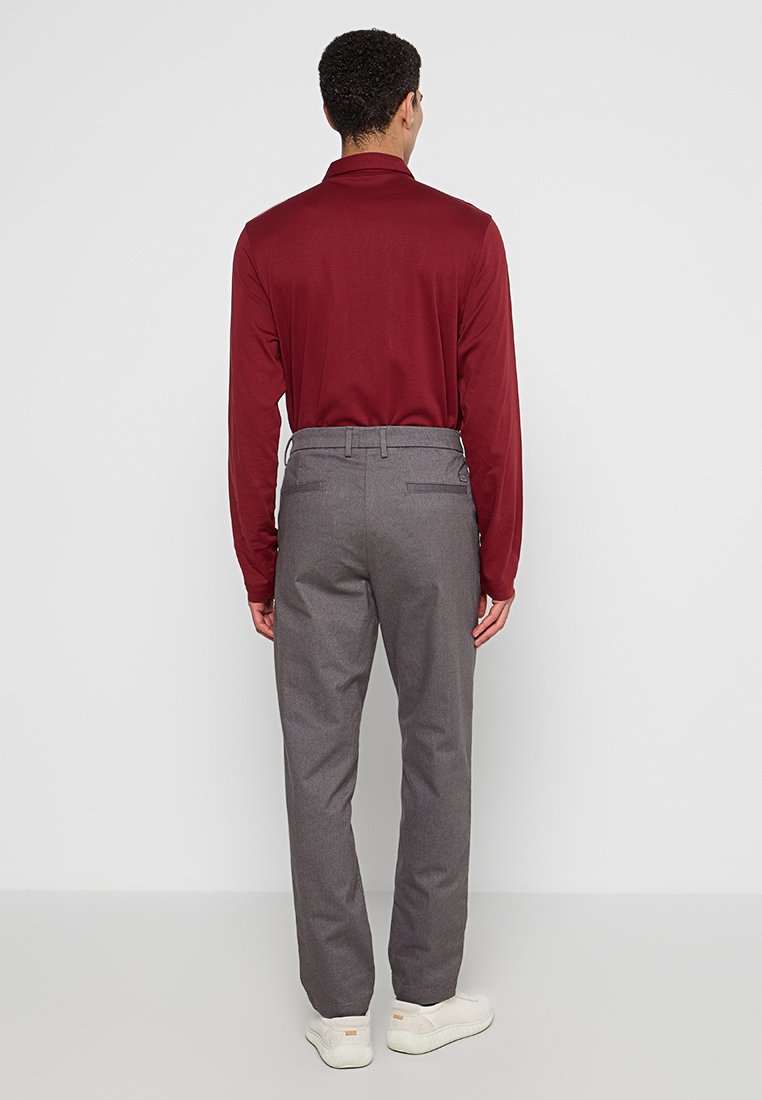 Graue Hose mit schmaler Passform, ausgestattet mit Gesäßtaschen und Gürtelschlaufen, kombiniert mit einem burgunderfarbenen Langarmoberteil. Glatte Stofftextur.