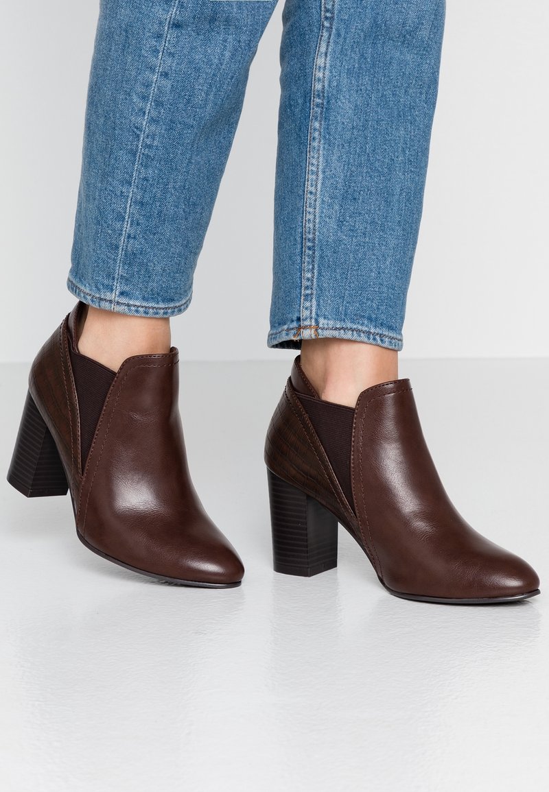 Botas de tobillo de cuero marrón con punta afilada y acentos laterales texturizados. Cuentan con un tacón ancho y paneles elásticos para facilitar su uso.