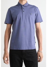 Polo tričko s krátkým rukávem v jemné fialové barvě, vybavené klopovým límečkem na tři knoflíky a vyšitým logem na hrudi. V kombinaci s černými kalhotami.