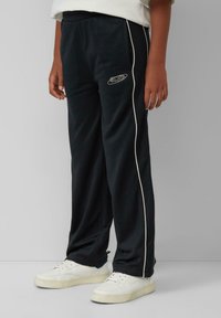Zwarte joggerbroek met witte zijpiping en logo. Gemaakt van een zachte stof. Gecombineerd met witte sneakers met geperforeerde accenten.