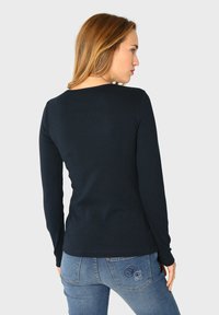 Granatowa koszula z długim rękawem o dopasowanym kroju, gładkiej fakturze i okrągłym dekolcie, w połączeniu z niebieskimi dżinsami z haftowanymi detalami na kieszeniach.