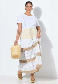 Longuette bianca in pizzo con fascia in maglia beige, caratterizzata da dettagli a motivo marrone. Abbinata a una semplice t-shirt bianca e una borsa in tessuto intrecciato.