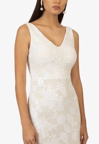 Weißes Spitzenkleid mit V-Ausschnitt und ärmellosem Design. Verfügt über bestickte Blumenmuster und eine figurbetonte Silhouette.