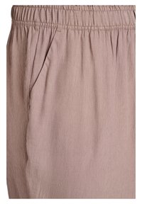 Tessuto rosa chiaro, spiegazzato, con una vita elasticizzata. Presenta tasche laterali e una texture sottile, creando una vestibilità rilassata.