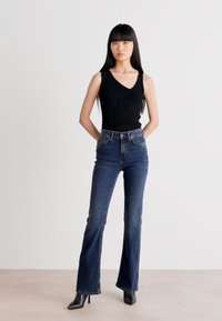 Svart ermeløs topp, høyt liv mørkeblå flared jeans og svarte spisse hæler. Glatt stoff med subtile sømdetaljer.