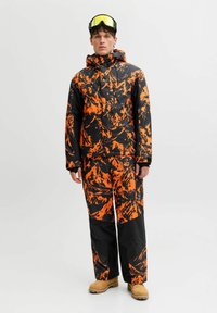 Mono de esquí con un patrón negro y naranja, fabricado en material impermeable. Incluye capucha y múltiples bolsillos para mayor funcionalidad.
