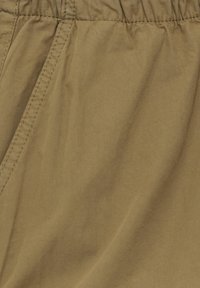 Gros plan sur un tissu kaki avec une ceinture élastique et des coutures visibles le long de la couture.