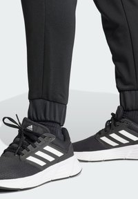 Czarne buty sportowe z białymi paskami i akcentami, z siateczkową cholewką, amortyzującymi podeszwami i elastycznymi spodniami zwężającymi się ku dołowi.