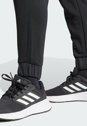 Schwarze Sportschuhe mit weißen Streifen und Akzenten, ausgestattet mit einem Mesh-Obermaterial, gepolsterten Sohlen und elastisch tapering Hosen.
