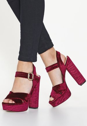 Fuchsia velvet platform sandals with a crocodile texture, ankle strap featuring a metallic buckle, and a chunky high heel.