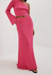 Sovitettu, ribattu neulekahden osan asu elävässä pinkissä. Yläosassa on yksi olka ja kellotettu hihapituus; hame on pitkä lattiaan saakka ja suora siluetti.