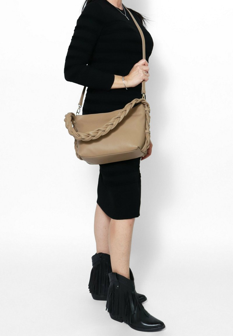 Borsa a spalla in pelle beige con tracolla intrecciata, texture morbida, forma rettangolare e fondo piatto, tenuta da una persona che indossa un vestito nero aderente.