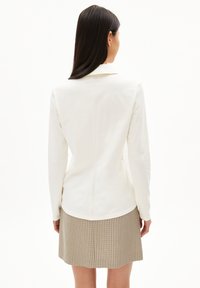 Witte blouse met lange mouwen en kraag, getailleerde pasvorm en detail aan de achternaad, gecombineerd met een geruite rok in tinten beige en bruin.
