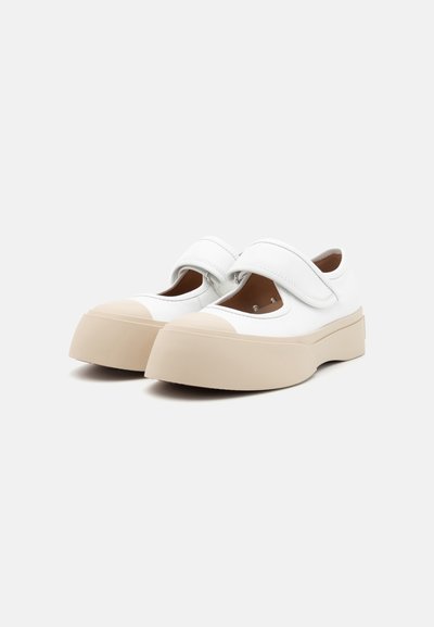 Sapatos Mary Jane brancos com bico arredondado, fita de velcro e sola bege grossa. Parte superior em couro liso com detalhes recortados para ventilação.
