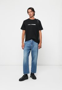Black cotton t-shirt with white logo, light blue denim jeans with straight cut, and black sneakers. Simple, modern design.