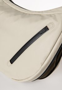 Beige Nylon-Schultertasche mit runder Form. Verfügt über eine schwarze Reißverschlusstasche und nahtloses Nähen entlang der Kanten.