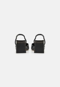 Black leather heeled sandals with square block heels, open back, and rounded toe design. Smooth texture with minimal detailing.