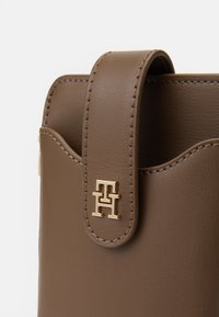 Geantă din piele maronie, cu închidere tip clapetă și accesorii din metal de culoare aurie. Prezintă margini curbate și detalii de coasere vizibile.