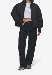 Giacca nera imbottita con colletto alto, design corto e polsini a costine, abbinata a jeans neri a vita alta e sneaker grigie.