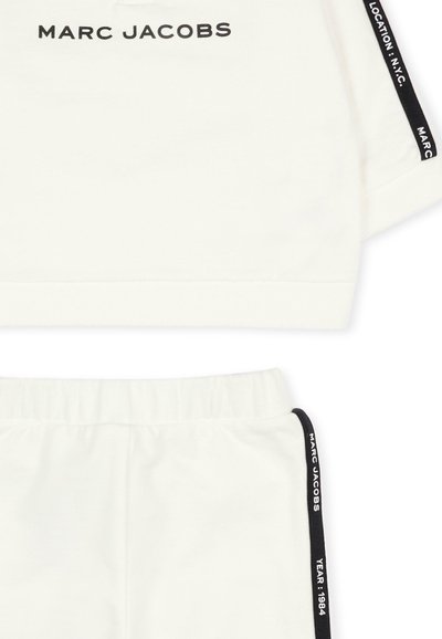 Witte stoffen set met een shirt met korte mouwen waarop het zwarte "MARC JACOBS" logo staat, en bijpassende shorts met zwarte accenten aan de zijkanten en tekstdetails.