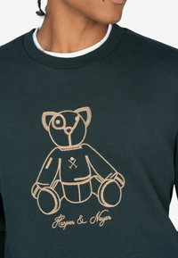 Donkergroen sweatshirt met een gouden geborduurd berenontwerp en de tekst "Harper & Nayer" onderaan. Ronde hals en textuurstof.